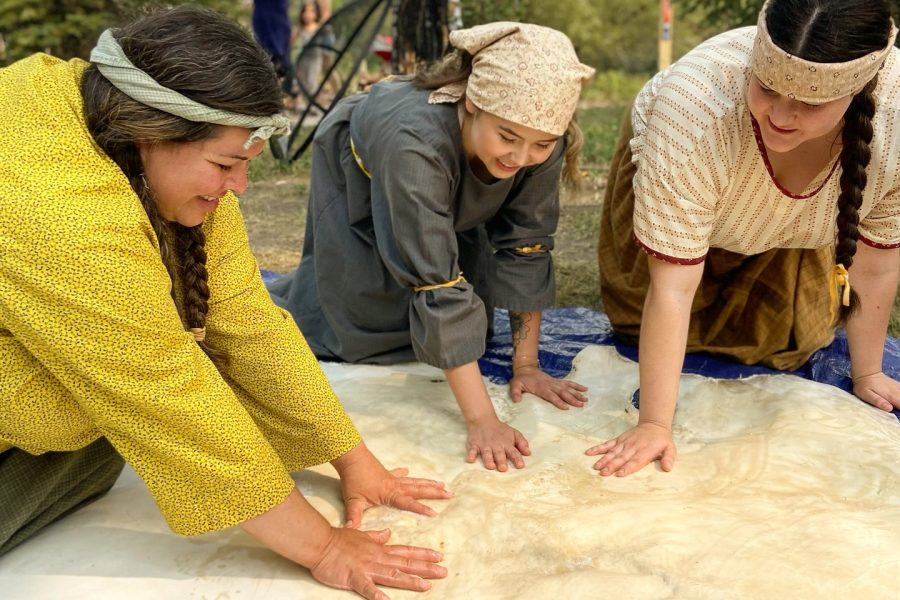 Three interpreters are working on brain tanning a hide at the Indigenous Peoples Experience at Fort Edmonton Park.