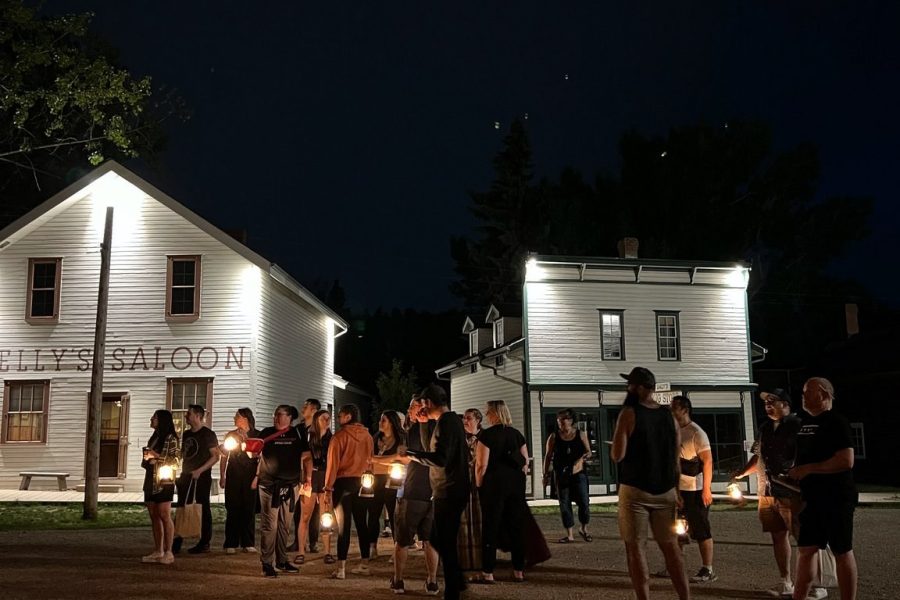 A crowd is visible on 1885 Street, in front of Kelly's Saloon. It is dark out with only their lanterns lighting the street.